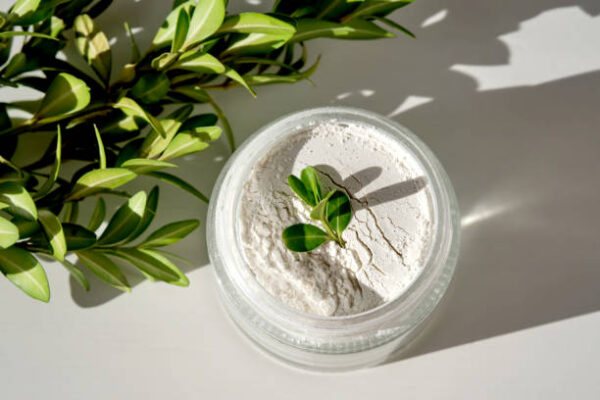An open jar of facial scrub powder with a green sprig.