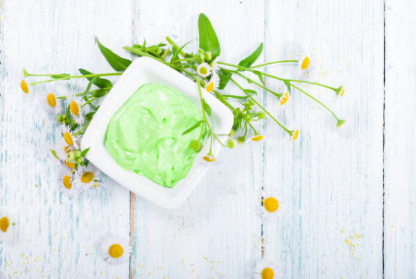 Green cosmetis cream with chamomile flowers on white wooden table