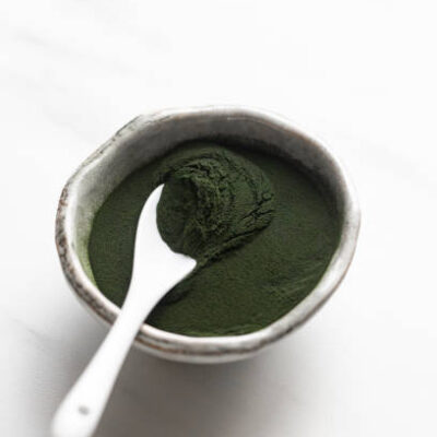 Organic spirulina powder in rustic bowl on white marble background